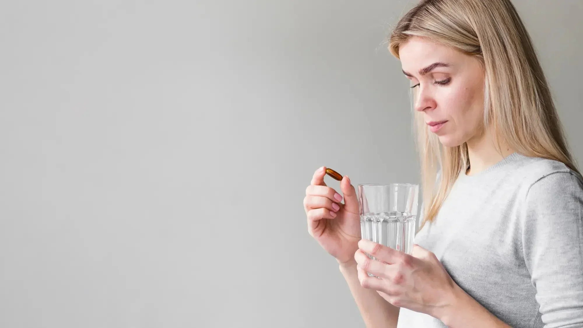 Femme tenant une gélule et un verre d'eau, illustrant la prise d'un complément alimentaire en zinc