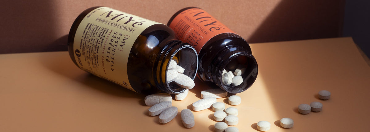 Deux piluliers renversés dont l'un sort des comprimés à croquer et l'autre des gélules de compléments alimentaires pour l'équilibre hormonal féminin