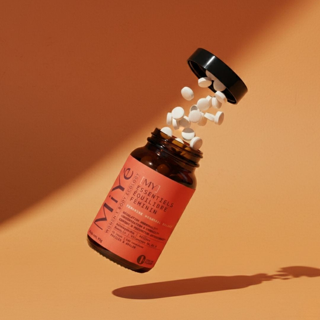 Un pilulier [MY] Essentiels équilibre féminin avec le couvercle et les comprimés qui s'envolent